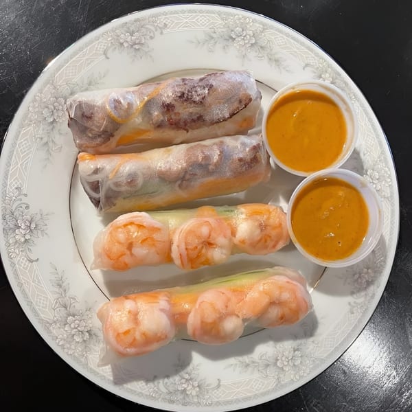 Four fresh spring rolls, two shrimp and two beef, with two cups of peanut sauce on a white plate.