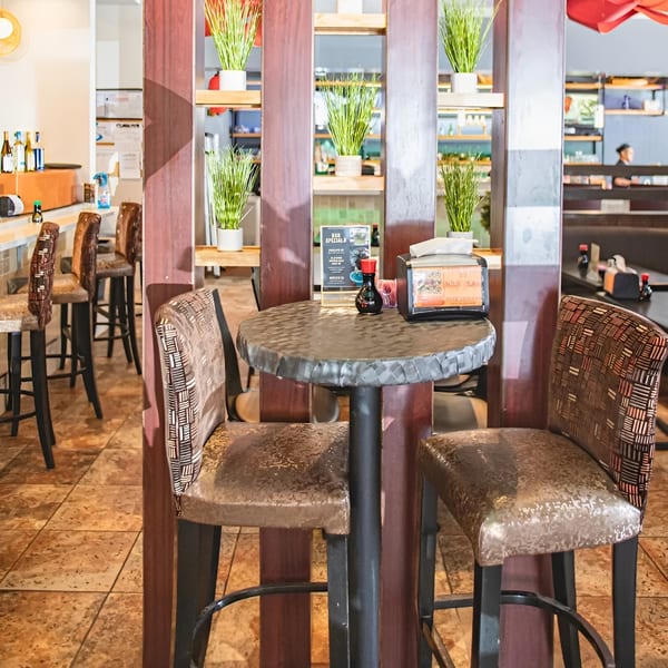 A small round table with two bar stools, soy sauce, and a napkin dispenser at Zake.
