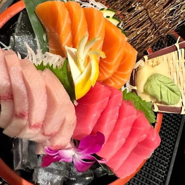 A colorful sashimi platter with salmon, tuna, and yellowtail, garnished with lemon, wasabi, and a purple orchid.
