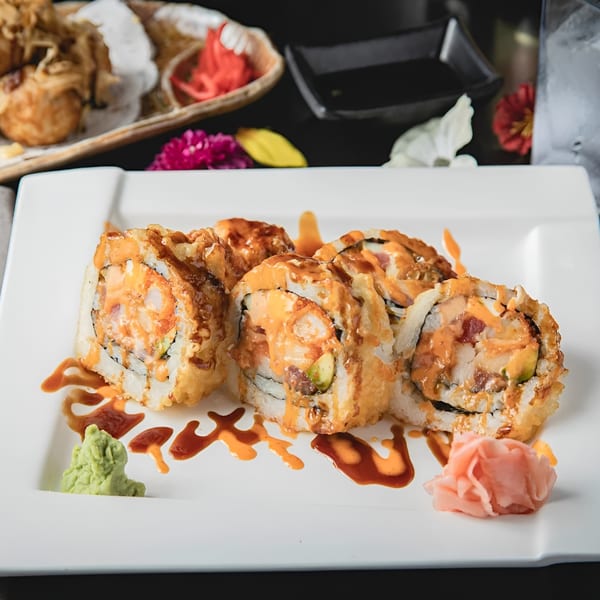 Six pieces of Zake's fried sushi rolls with sauce, wasabi, and pickled ginger on a white plate.