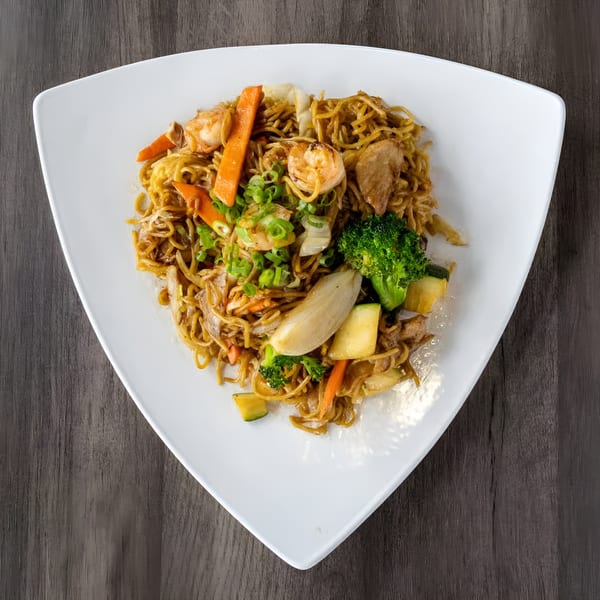 Zake's Asian-fusion noodles with shrimp, chicken, broccoli, carrots, and zucchini on a white plate.