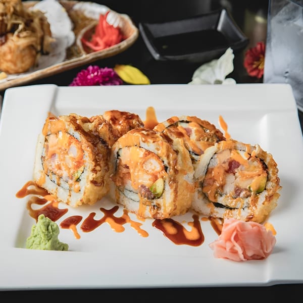 Six pieces of Zake's fried sushi rolls with sauce, wasabi, and pickled ginger on a white plate.