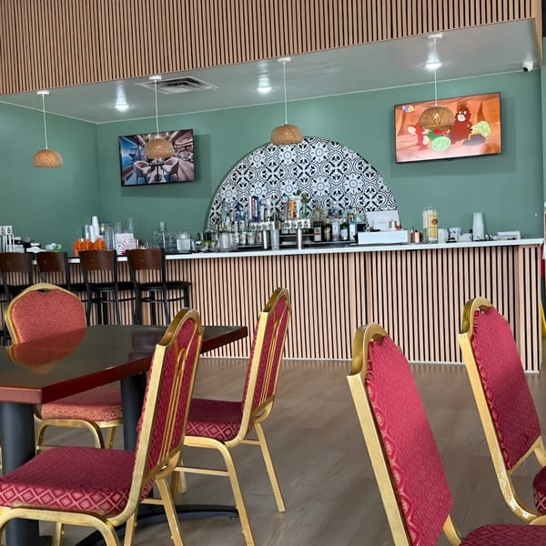 Zake's dining area with red chairs, dark tables, a bar with patterned tiles, and light green walls.