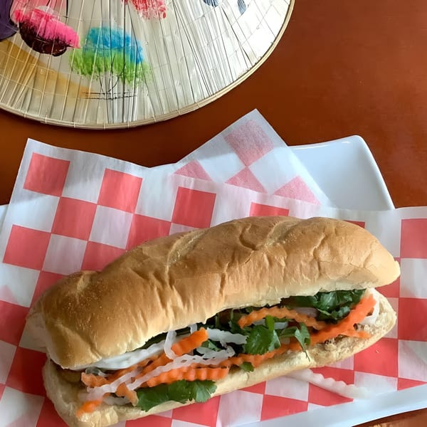 Zake's banh mi sandwich with pickled carrots, daikon, and cilantro on red checkered paper.