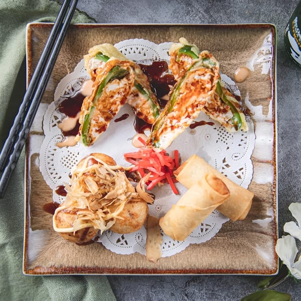A Zake appetizer platter with tempura, takoyaki, spring rolls, and pickled ginger on a decorative plate.